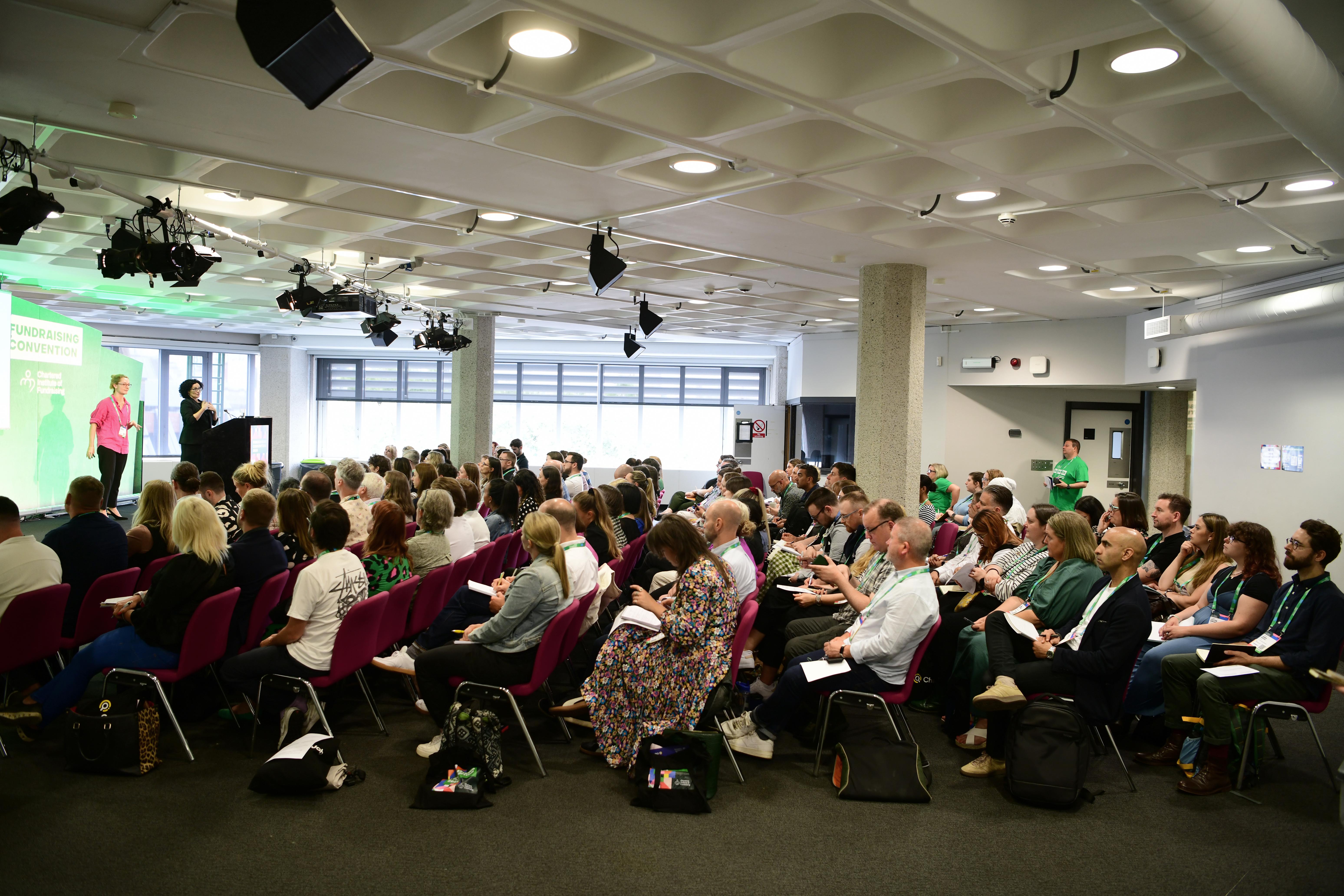 A group of fundraisers sitting in a rows of chairs facing the front with a person at the front speaking to them