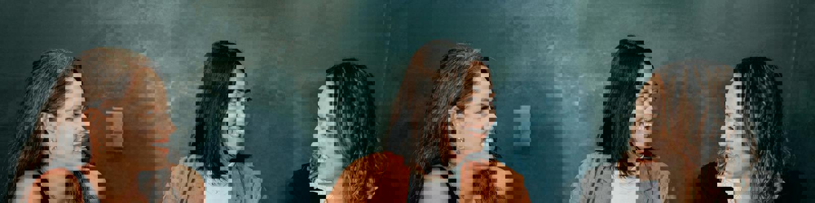 Three women working around a laptop in an office, with a dark background