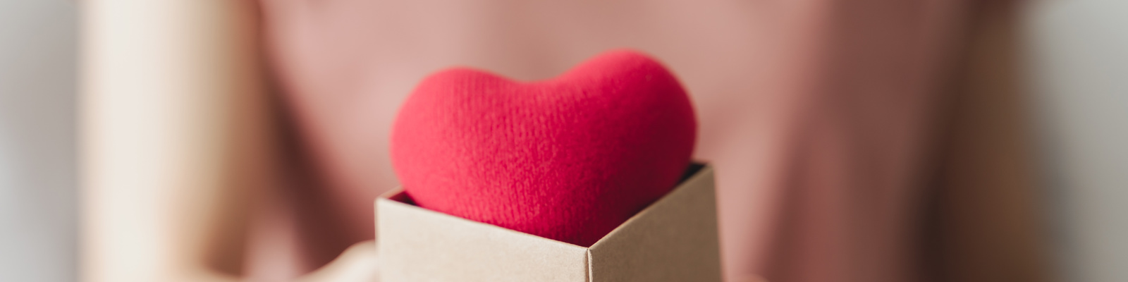 Woman holding a giftbox with a red heart inside of it. Symbolising donation and giving with love and care.