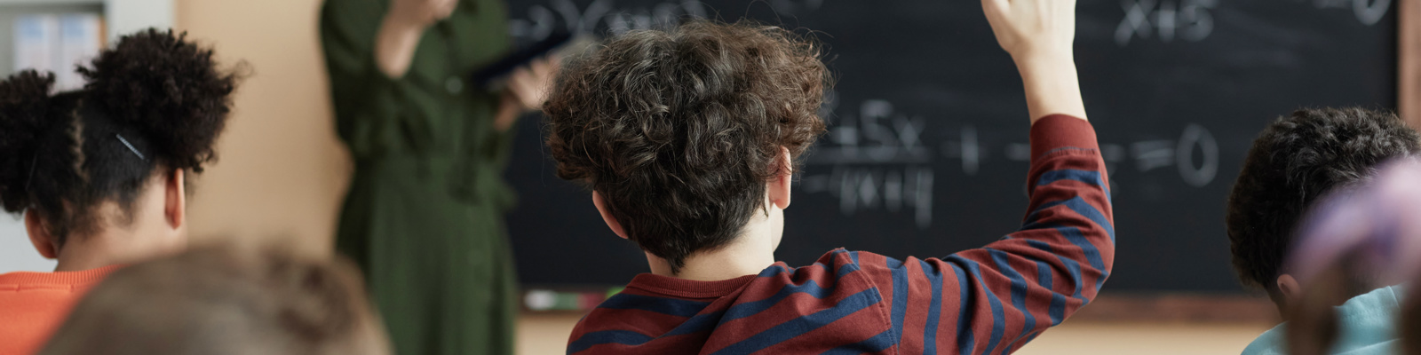 Back view at group of children raising hands in school classroom and participating in discussion