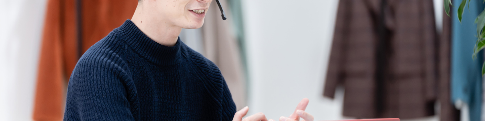 Person in a dark navy jumper wearing a headset whilst typing on a laptop with a pink cover in a modern workspace