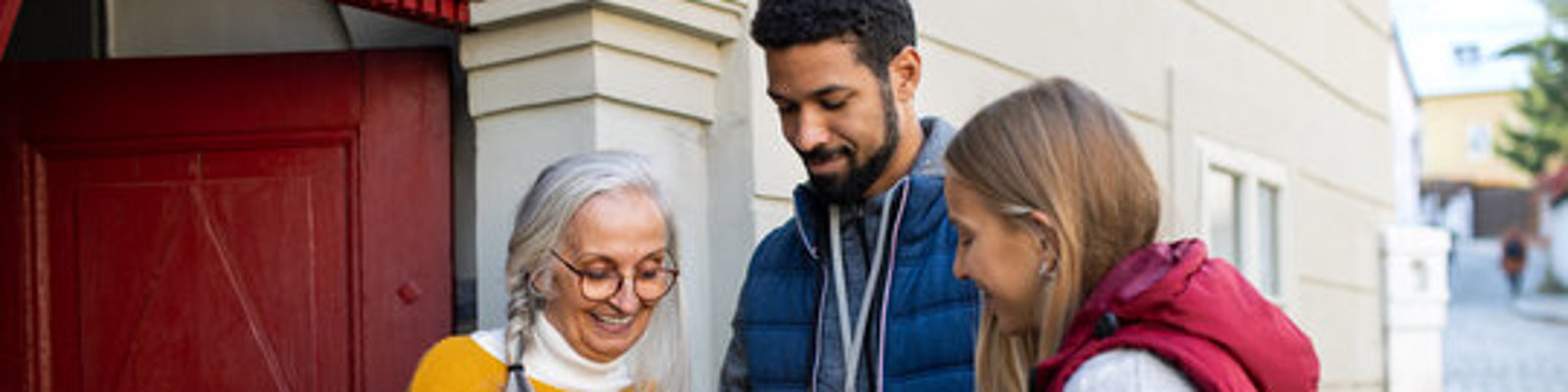 Young door to door fundraisers talking to senior woman and collecting money for charity in street.