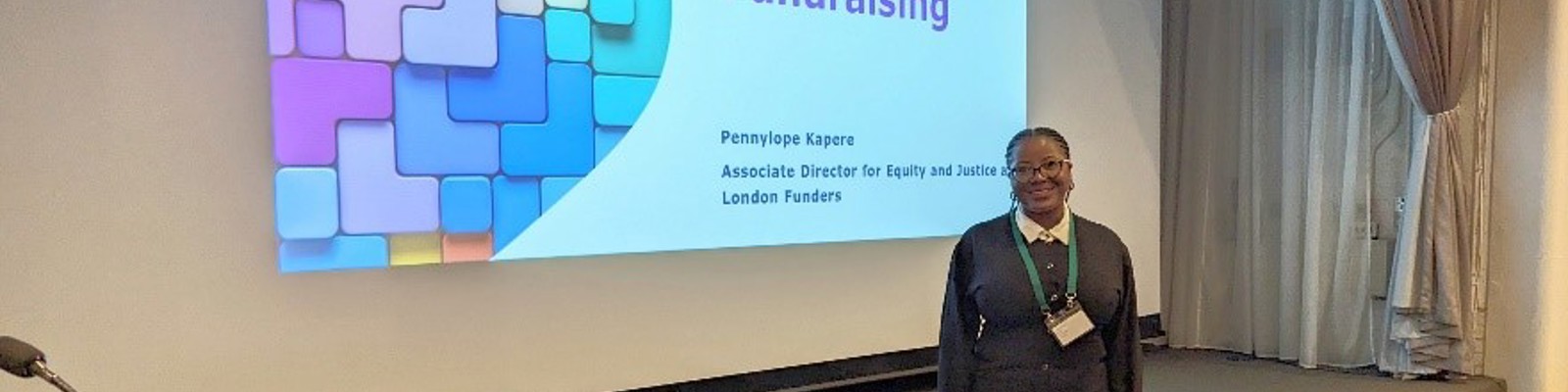 Photo of Pennylope T. Kapere standing in front of a presentation screen smiling.
