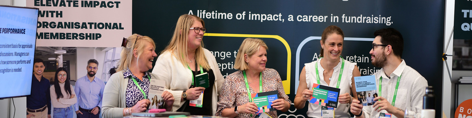 The CIOF team standing and sitting infront of a banner holding up leaflets