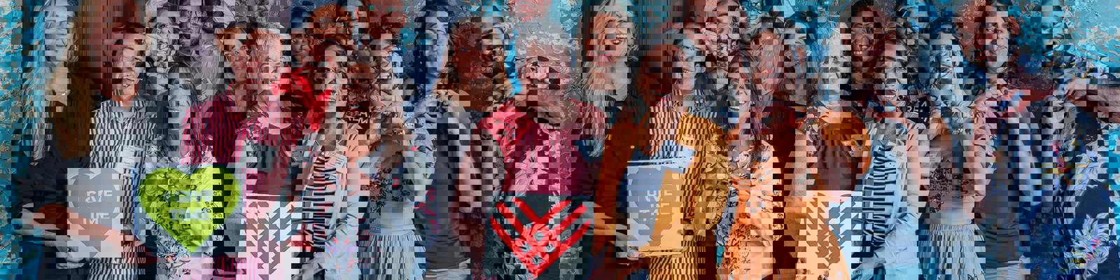 A photo of a group of people holding photos of the Giving Tuesday Logo, one man doing a heart shape with his hand, and one poster saying 'I Give Time'