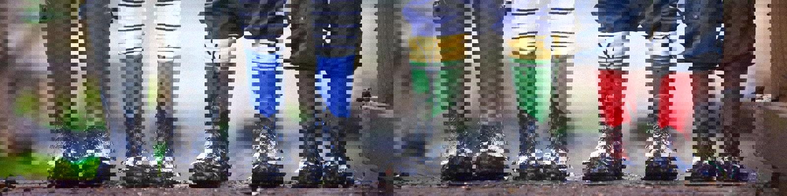 Photo of 3 children and adult legs, showing their wellington boots muddy on a trail.