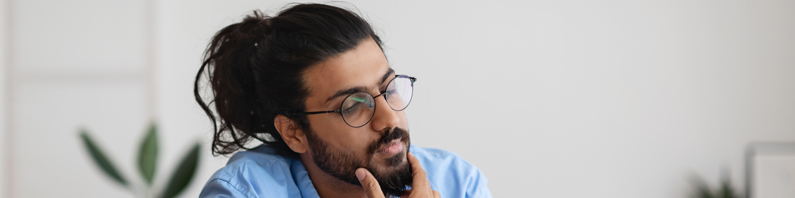 Man in glasses and a light blue shirt with his hand on his chin looking thoughtfully at documents whilst working from home