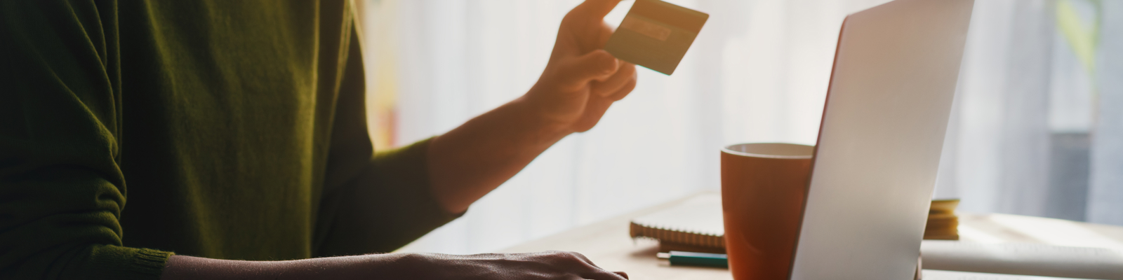 Photo of a Woman Holding Up a Debit Card Entering the Details into a Laptop.