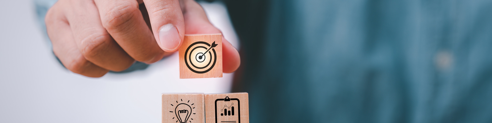 Photo of a hand stacking wood blocks on table with icons that represent a business strategy and action plan.