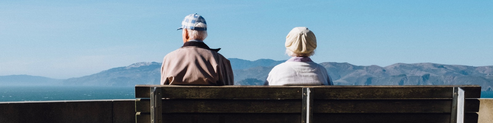 Photo of an older man and woman sitting on a bench overlooking a mountain view.