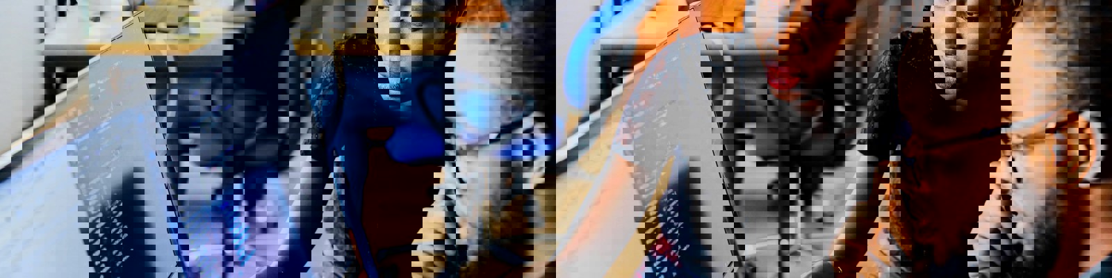 Two black people sit at a desk looking at a computer with data on the screen. 