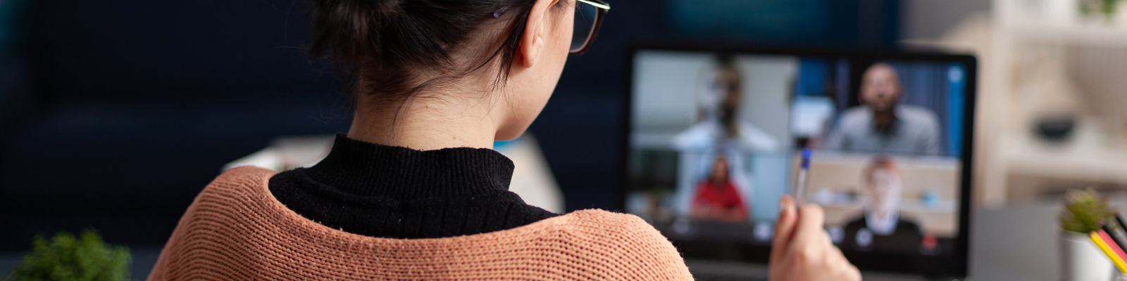 Rear view of woman in an orange jumper participating in a video conference call on her laptop at home