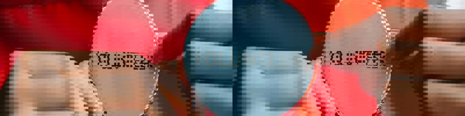 A woman in a red top holds a pin badge which has the word volunteer printed on it